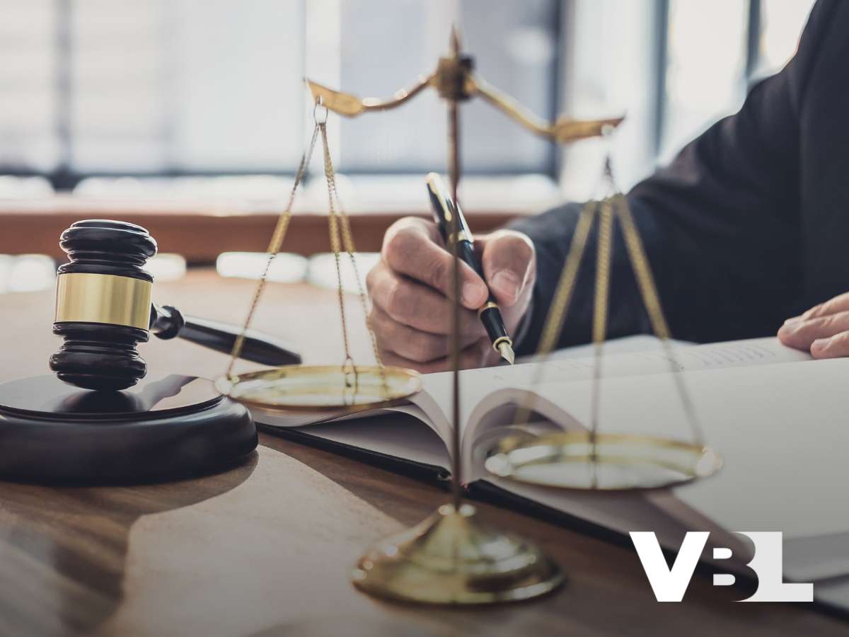 Gavel and scales of justice on a desk with a person writing, representing legal aspects of Bankruptcy.